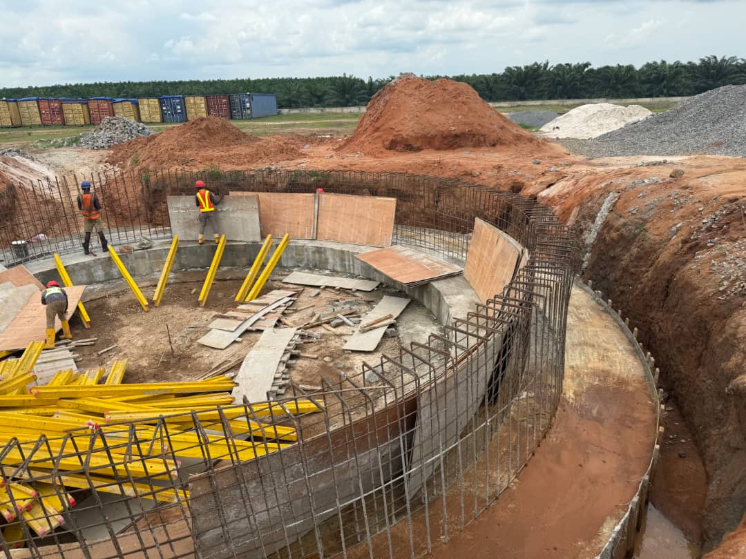 Workers fixing rebar and shuttering inside a deep circular tank excavation