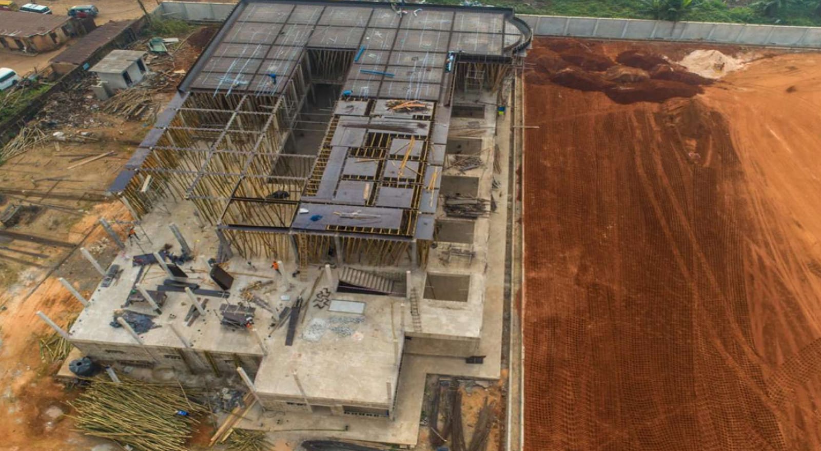 Aerial view of the terminal building's columns and floor slabs beside graded red earth