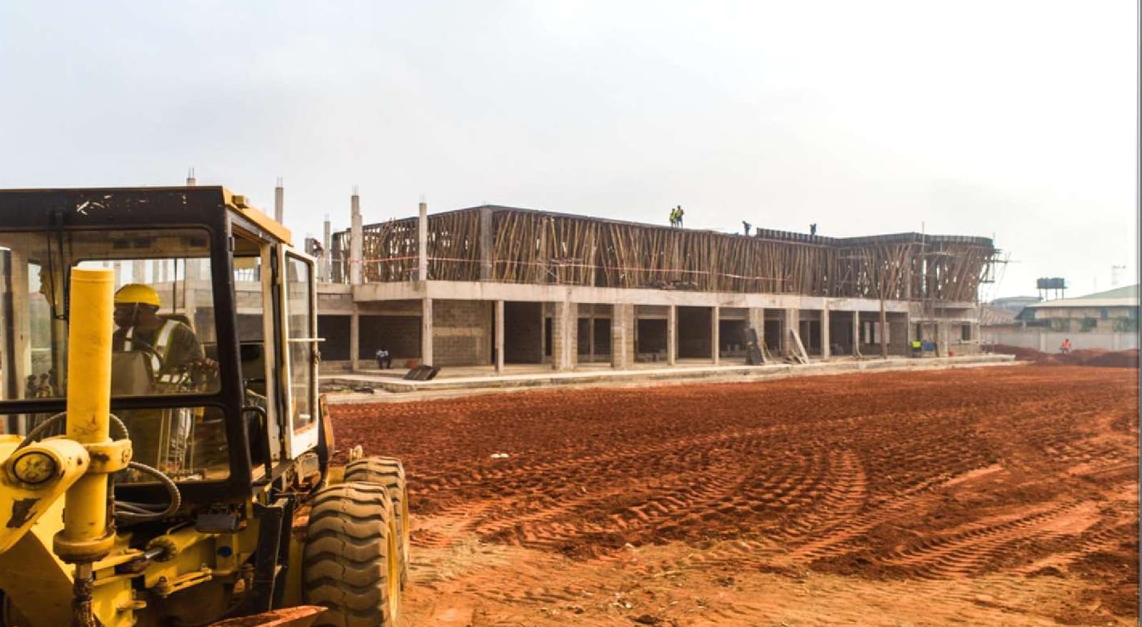 Motor grader levelling the ground beside the rising terminal building frame
