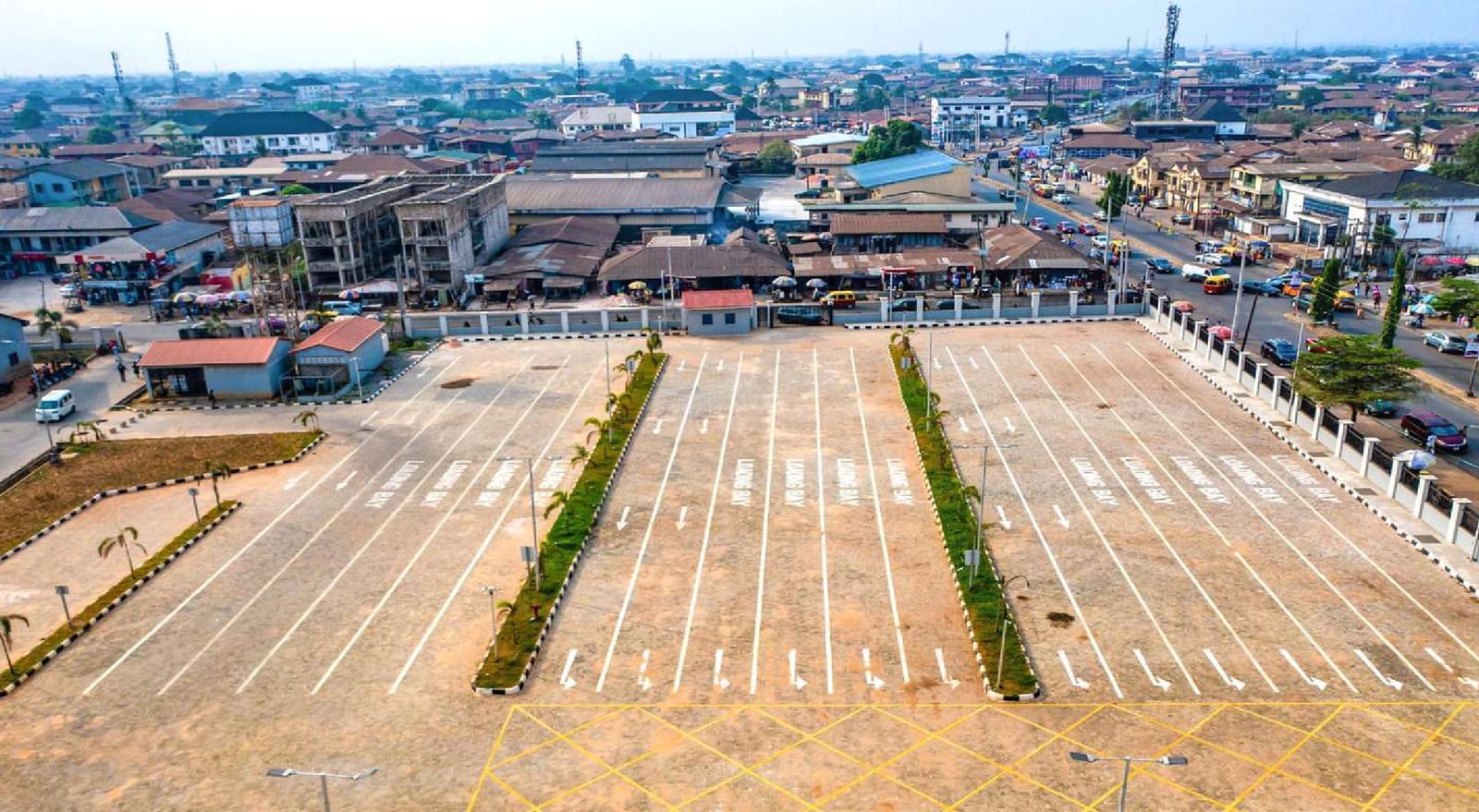 Aerial view of paved parking bays separated by planted medians with the Benin City skyline behind